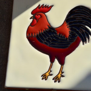 Può includere: Un gallo rosso e nero su sfondo bianco. Il gallo è dipinto in stile folk.