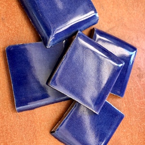 May include: Four blue ceramic tiles with a glossy finish. The tiles are arranged in a pile, with the top tile slightly offset from the others.