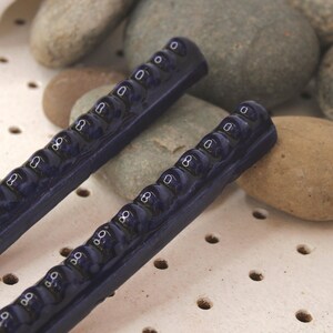May include: Two dark blue hair clips with a series of numbers printed on them. The clips are made of ceramic and have a glossy finish.