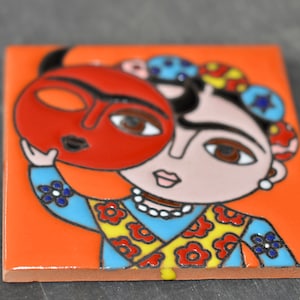 May include: A colorful ceramic tile featuring a cartoon illustration of a woman with a red mask over her face. The woman is wearing a blue and yellow patterned shirt with red flowers. The background is orange.