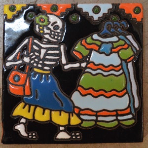 Puede incluir: Un azulejo de cerámica colorido con un esqueleto que lleva un vestido azul y amarillo y lleva un bolso rojo, de pie junto a un vestido a rayas con un lazo azul.