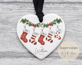Può includere: Ciondolo in ceramica bianco a forma di cuore con una ghirlanda verde e cinque calze appese. Le calze sono rosse e bianche con i nomi scritti su di esse: Mark, Louise, Isabella, Luke e Teddy. Il ciondolo ha anche il testo "The Willson Family" scritto su di esso.