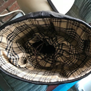 May include: The inside of a black leather bag with a plaid lining. The lining is a black and white plaid pattern.