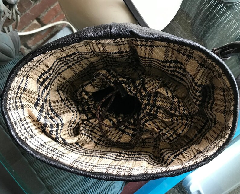 May include: The inside of a black leather bag with a plaid lining. The lining is a black and white plaid pattern.