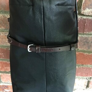 May include: Black leather crossbody bag with a brown leather strap and buckle. The bag has a flap closure and a slouchy design.