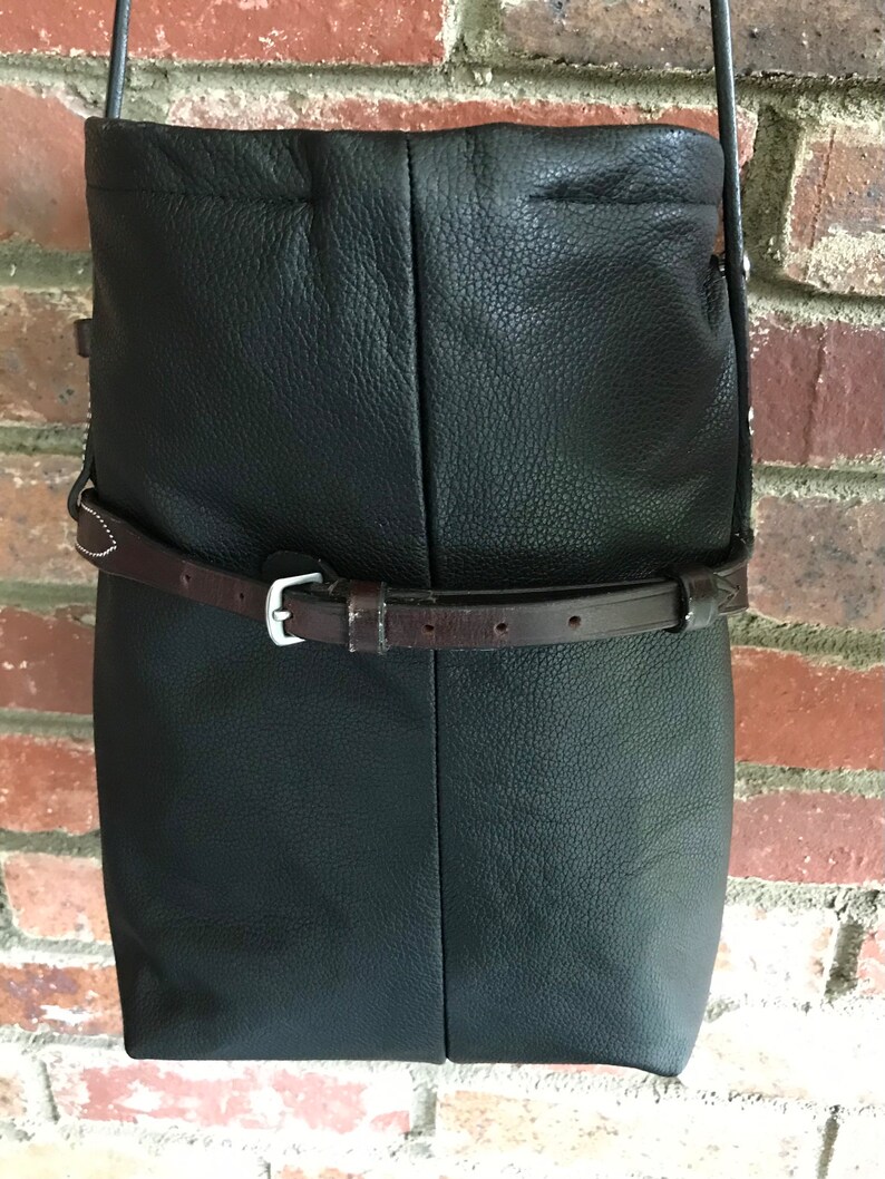 May include: Black leather crossbody bag with a brown leather strap and buckle. The bag has a flap closure and a slouchy design.
