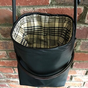 May include: A black leather bucket bag with a plaid fabric lining. The bag has a brown leather strap and a top handle.