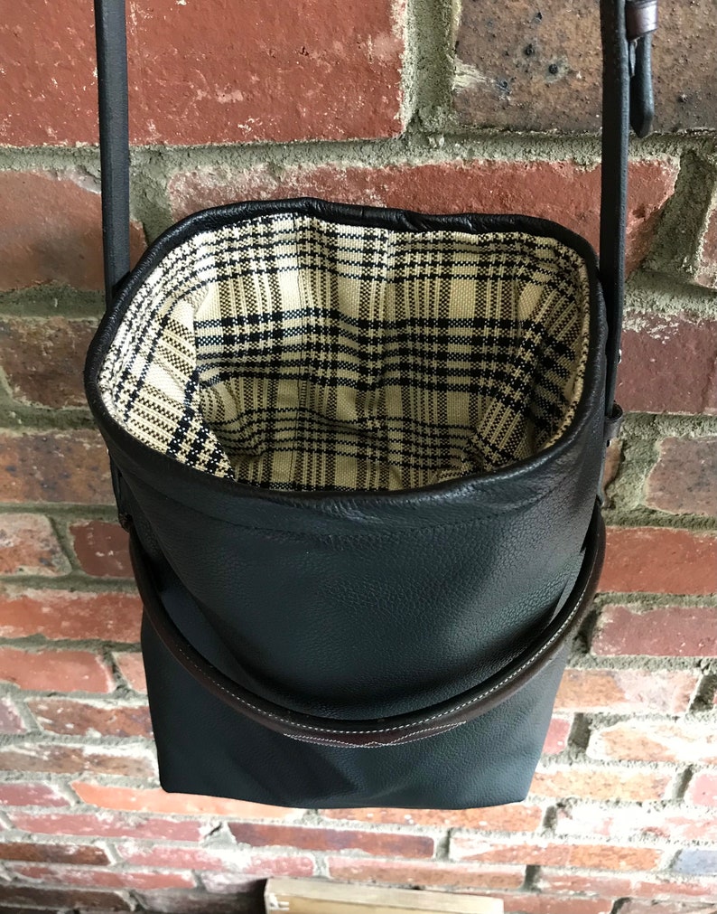 May include: A black leather bucket bag with a plaid fabric lining. The bag has a brown leather strap and a top handle.