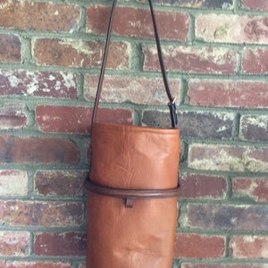 May include: A brown leather bucket bag with a black strap. The bag has a brown leather trim around the top.