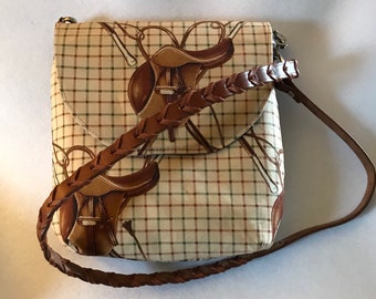 May include: A brown and beige plaid crossbody bag with a brown braided strap. The bag features a repeating pattern of brown saddles and bridles.