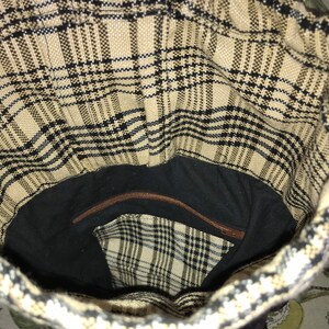 May include: The inside of a brown and black plaid tote bag with a zippered pocket. The bag is lined with black fabric.