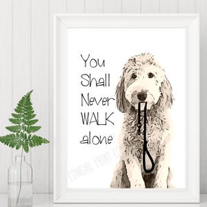 Op de afbeelding: Een witte ingelijste print met een zwart-witte illustratie van een hond die een riem in zijn bek houdt. De tekst "You shall never walk alone" is onder de hond gedrukt.