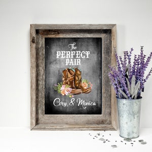 May include: Framed rustic artwork with the text "The Perfect Pair" above a watercolor illustration of cowboy boots and flowers. The names "Cory, & Monica" are below the boots. A galvanized metal vase holds lavender.