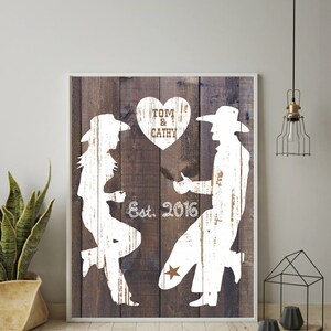 May include: White silhouette of a couple in cowboy hats, with the woman on one knee and the man standing, on a rustic wood background. The text "TOM & CATHY" is in a heart shape above them, and "Est. 2016" is below them.