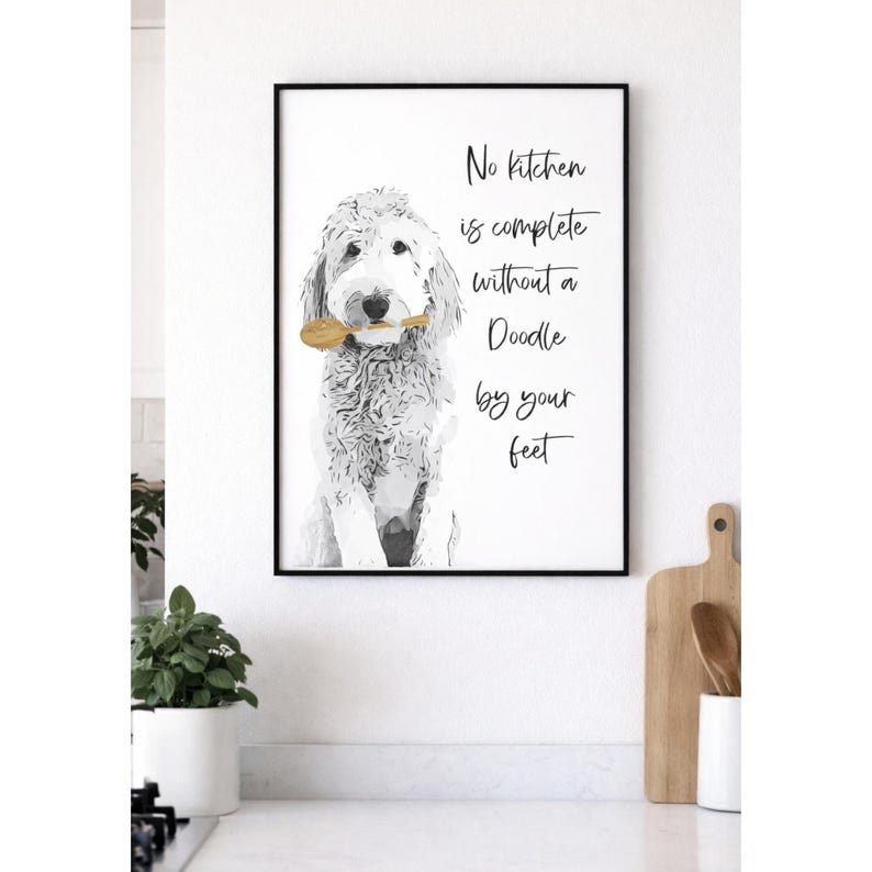Puede incluir: Una l&aacute;mina decorativa enmarcada con una ilustraci&oacute;n en blanco y negro de un perro Goldendoodle sosteniendo una cuchara de madera en la boca. El texto dice: No kitchen is complete without a Doodle by your feet. El marco es negro y fino.