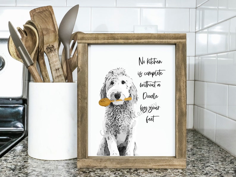 May include: A framed print with a black and white illustration of a doodle dog holding a wooden spoon. The text on the print reads "No kitchen is complete without a Doodle by your feet."