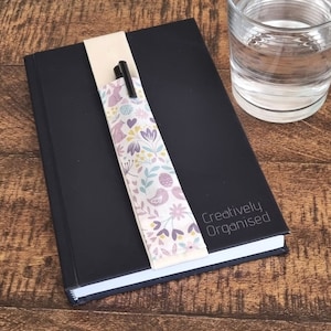 May include: A black notebook with a floral patterned pen holder and the text "Creatively Organised" on the cover.