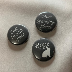 May include: Three dark gray buttons with white text and graphics. One button reads "Lost In Sub Space", another says "More Spankings Please", and the third has the word "Rope" with a rabbit silhouette.