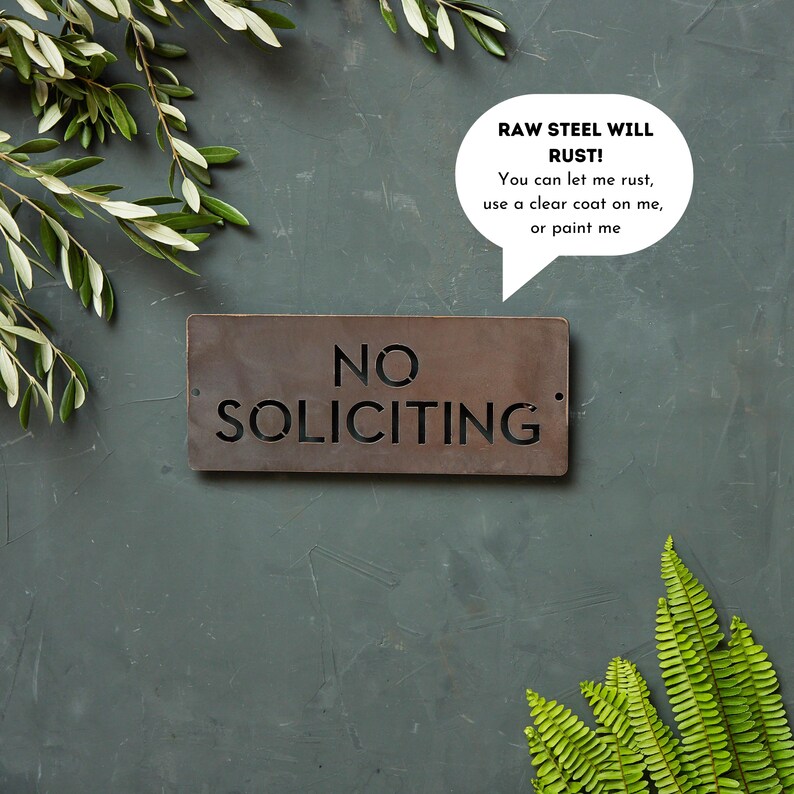 Op de afbeelding: Een rustiek metalen bord met de woorden "NO SOLICITING" in een uitgesneden ontwerp. Het bord is gemaakt van ruw staal en heeft een verweerde, roestige uitstraling. Een spraakballon boven het bord luidt "RAW STEEL WILL RUST! You can let me rust, use a clear coat on me, or paint me."