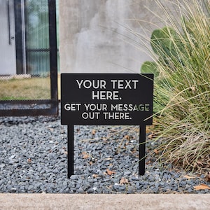 May include: Black metal sign with white text that reads "YOUR TEXT HERE. GET YOUR MESSAGE OUT THERE."