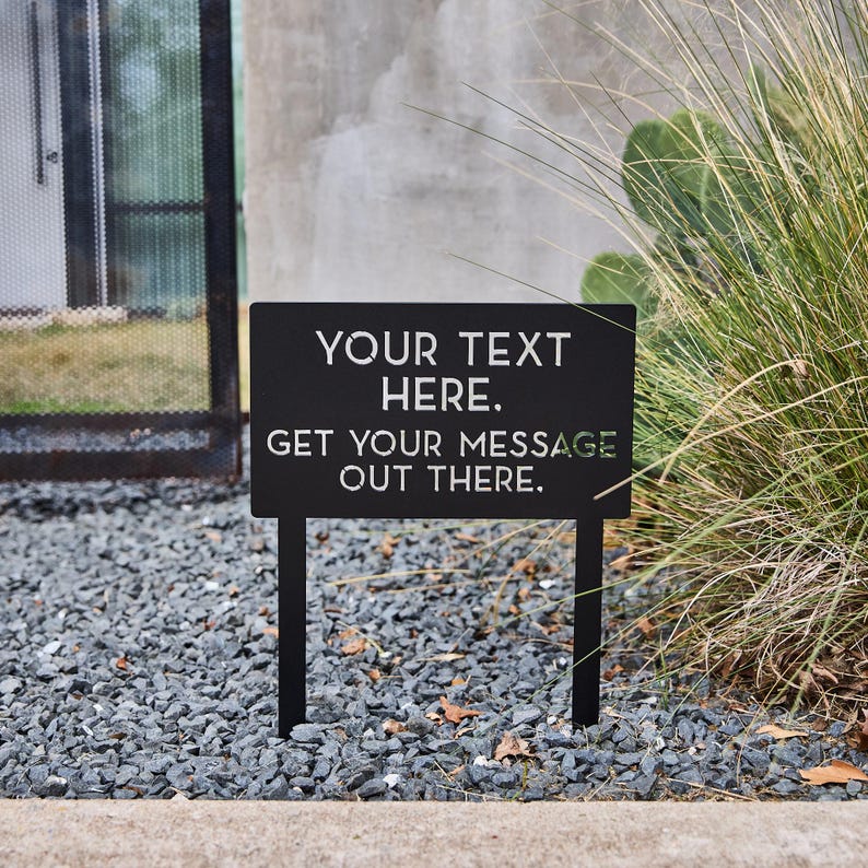 May include: Black metal sign with white text that reads "YOUR TEXT HERE. GET YOUR MESSAGE OUT THERE."