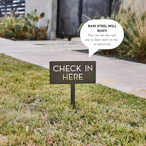 May include: A rectangular raw steel garden sign on a stake with the text CHECK IN HERE. A speech bubble above the sign reads: RAW STEEL WILL RUST! You can let me rust, use a clear coat on me, or paint me. The sign is dark gray and metallic.