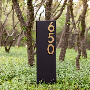 May include: A black sign with gold numbers reading "650" in a wooded area.