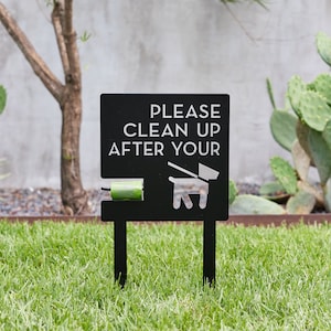 May include: Black metal sign with white text that reads "Please clean up after your" with a silhouette of a dog and a roll of green dog waste bags.