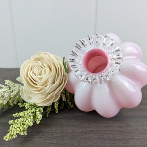 Può includere: Un vaso di vetro rosa con un bordo argentato a balze. Il vaso ha una forma bulbosa ed è perfetto per esporre piccoli fiori.