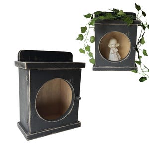 May include: Two black wooden decorative boxes with distressed finish. One box has a circular opening with a small door and a knob. The other box has a small figurine inside. Green vines are draped over the top of the second box.