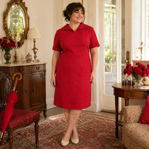 May include: A woman wearing a red, short-sleeved dress with a collared neckline. The dress has a subtle textured pattern. She is wearing beige heels. The background includes antique furniture, a mirror, and a red umbrella.