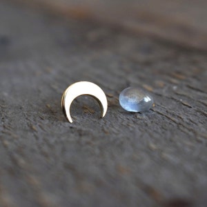 Può includere: Un ciondolo a forma di luna crescente dorato e una pietra cabochon in vetro trasparente su una superficie di legno.