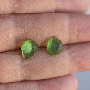 Pode incluir: Duas pequenas gemas verdes facetadas. As gemas têm uma forma irregular e são translúcidas.