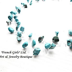 May include: A turquoise gemstone necklace with a clear string. The necklace is on a white surface. The text "French Girls" Ltd. Art & Jewelry Boutique is visible in the image.