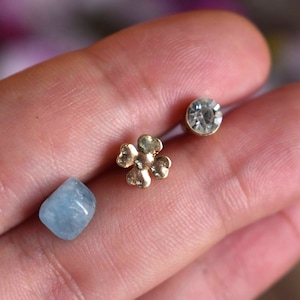 May include: Three small decorative items, a light blue stone, a gold four-leaf clover, and a clear rhinestone.