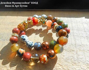 May include: Two bracelets made of colorful gemstone beads. The bracelets are layered on top of each other and feature a variety of colors, including red, orange, brown, green, and white. The beads are round and have a smooth, polished finish.