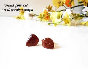 May include: Two small, brown, irregularly shaped stones with a glittery texture. The stones are likely used as earrings.