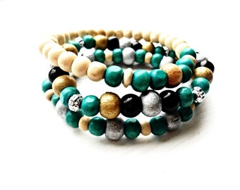 Può includere: Un set di tre braccialetti realizzati con perline di legno in tonalità beige, verde acqua, nero, oro e argento.