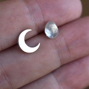 May include: A pair of silver earrings, one shaped like a crescent moon and the other a round, slightly iridescent stone.