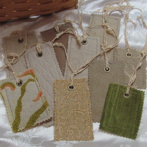 May include: A collection of fabric swatches with different textures and colors, including beige, brown, green, and white. Each swatch has a metal ring and a string attached.
