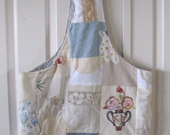 May include: A patchwork tote bag made from various fabrics in shades of white, cream, and blue. The bag features embroidered floral designs and lace accents. The bag has a long strap and is perfect for carrying everyday essentials.