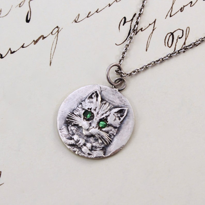 Handmade sterling silver coin with a cat wearing a bowtie engraving with green garnet eyes.