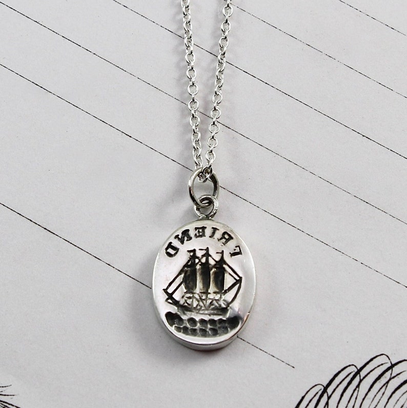 Sterling silver oval pendant carved with a ship design and "DNEIRF" on the top. Pendant hangs on a sterling silver cable chain.