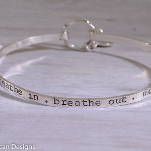 Puede incluir: Pulsera de brazalete de plata con la inscripción "breathe in. breathe out. move on".