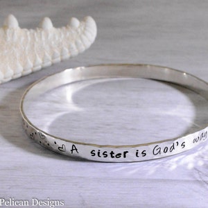May include: A silver bangle bracelet with the inscription "A sister is God's way of ..."