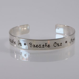 May include: Silver bracelet with the inscription "Breathe In * Breathe Out * Move On".