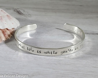 May include: Silver bangle bracelet with the inscription "The beautiful life is while you're in the moment".