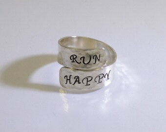 May include: A silver ring with the words "RUN HAPPY" engraved on it. The ring is designed to be worn on the knuckle.