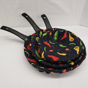 May include: Three black frying pans with a blue background and a pattern of red, yellow, and green chili peppers.