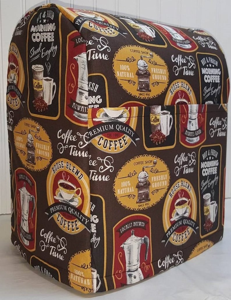 May include: A brown and yellow patterned fabric cover for a kitchen appliance. The cover features a coffee theme with images of coffee cups, coffee beans, and coffee grinders. The text on the cover reads "Coffee Time" and "Premium Quality Coffee".